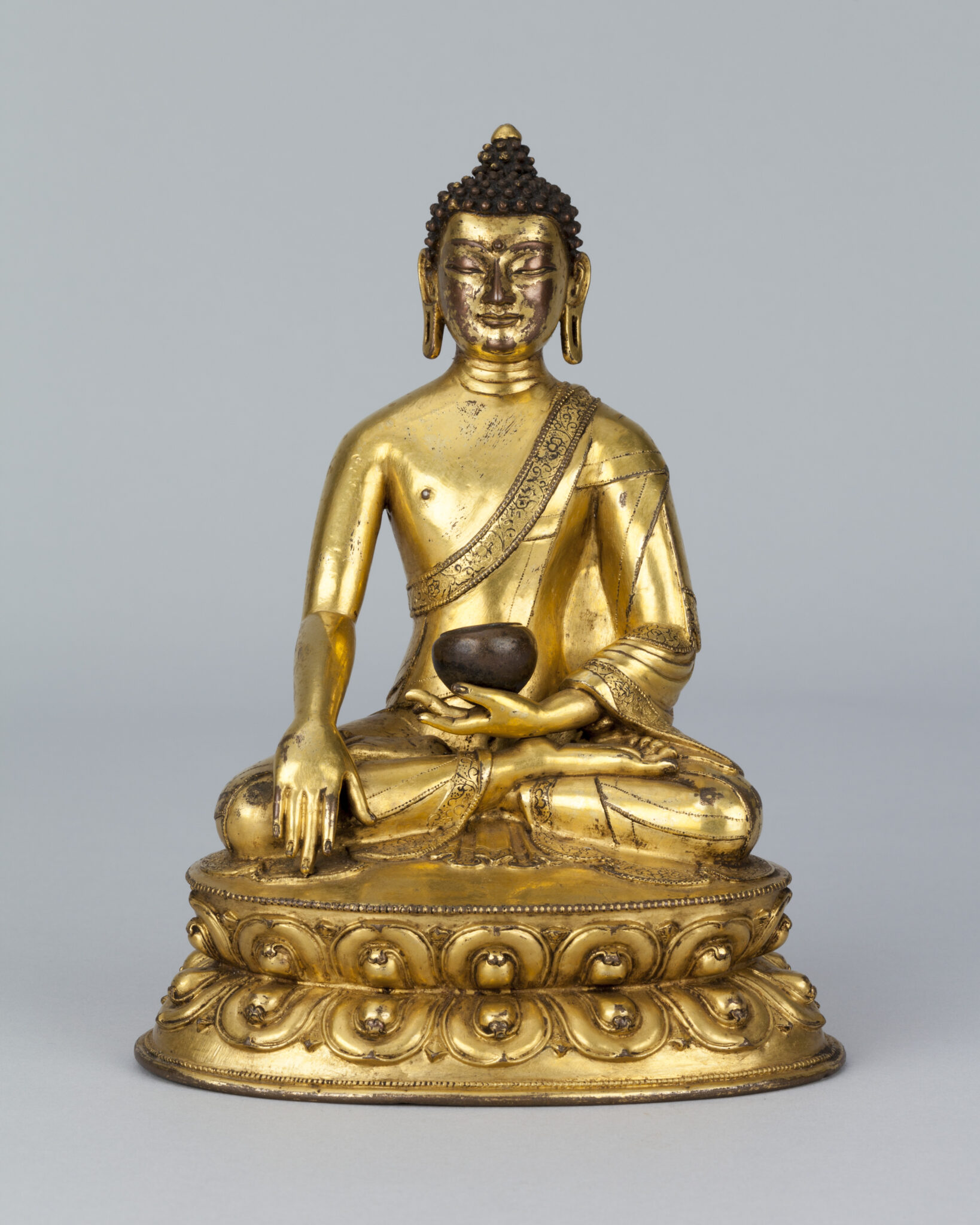 Golden statue depicting seated Buddha holding bowl in lap, left hand touching ground
