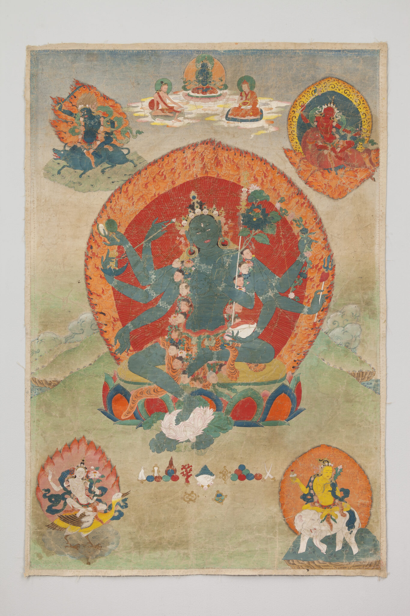 Green-skinned, many-armed Bodhisattva wearing garland of human heads seated before fiery nimbus