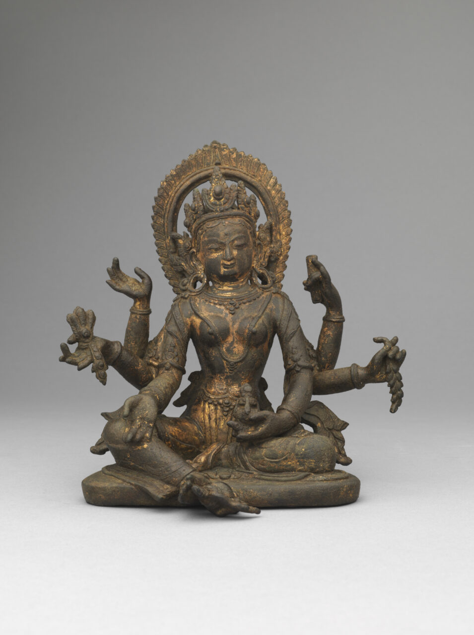 Tarnished copper-colored statue depicting six-armed goddess wearing pointed crown holding implements in each hand