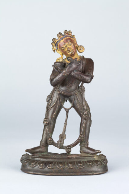 Patinated copper statue depicting deity standing with arms crossed at chest, wearing garland of human heads