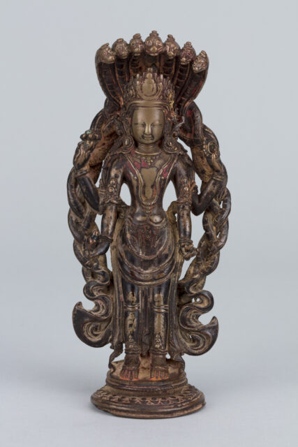Sculpture depicting deity flanked by braided bodies of serpents; head covered by hood of seven serpents