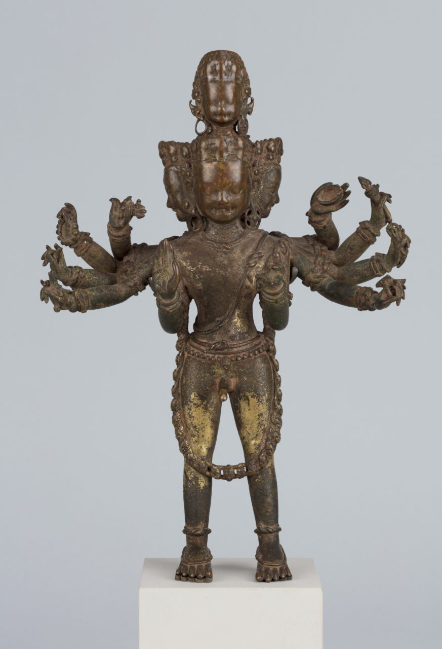 Tarnished copper sculpture depicting many-armed and -headed deity standing with feet planted firmly apart
