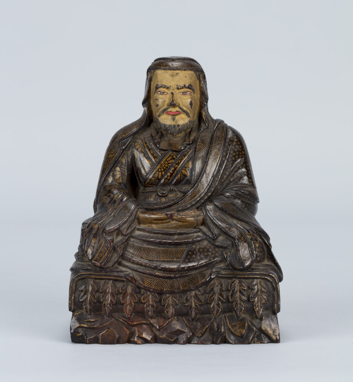 Polychrome sculpture depicting bearded Enlightened Teacher wearing pleated robes painted with floral motif at chest