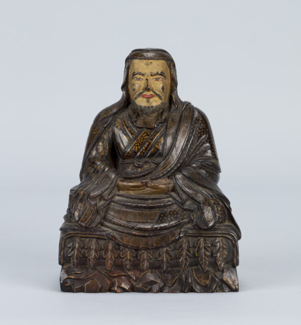 Polychrome sculpture depicting bearded Enlightened Teacher wearing pleated robes painted with floral motif at chest