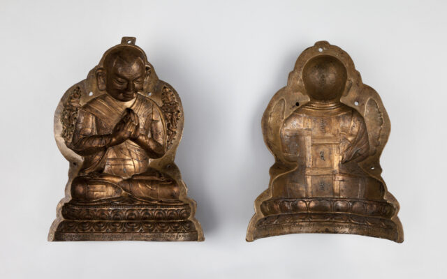 Two halves of bronze-colored mold used to produce sculpture depicting monk with hands at chest in prayer
