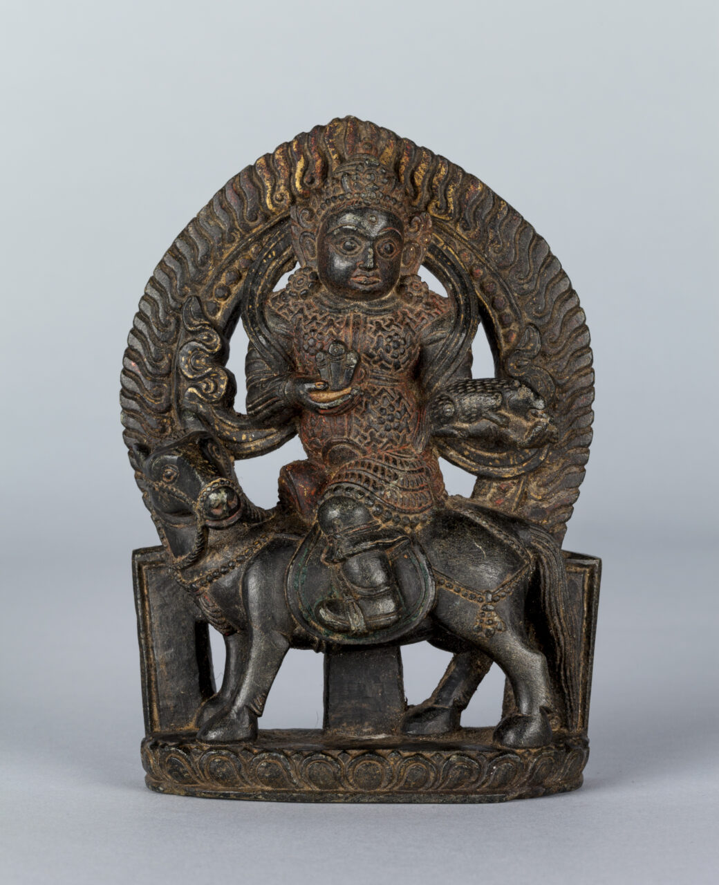 Dark brown sculpture with traces of gilding depicting deity riding on horseback before fiery nimbus