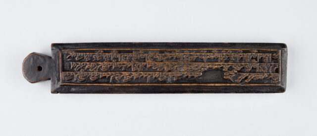 long, rectangular, ink-stained woodblock incised with dense text; handle with hole in center at left