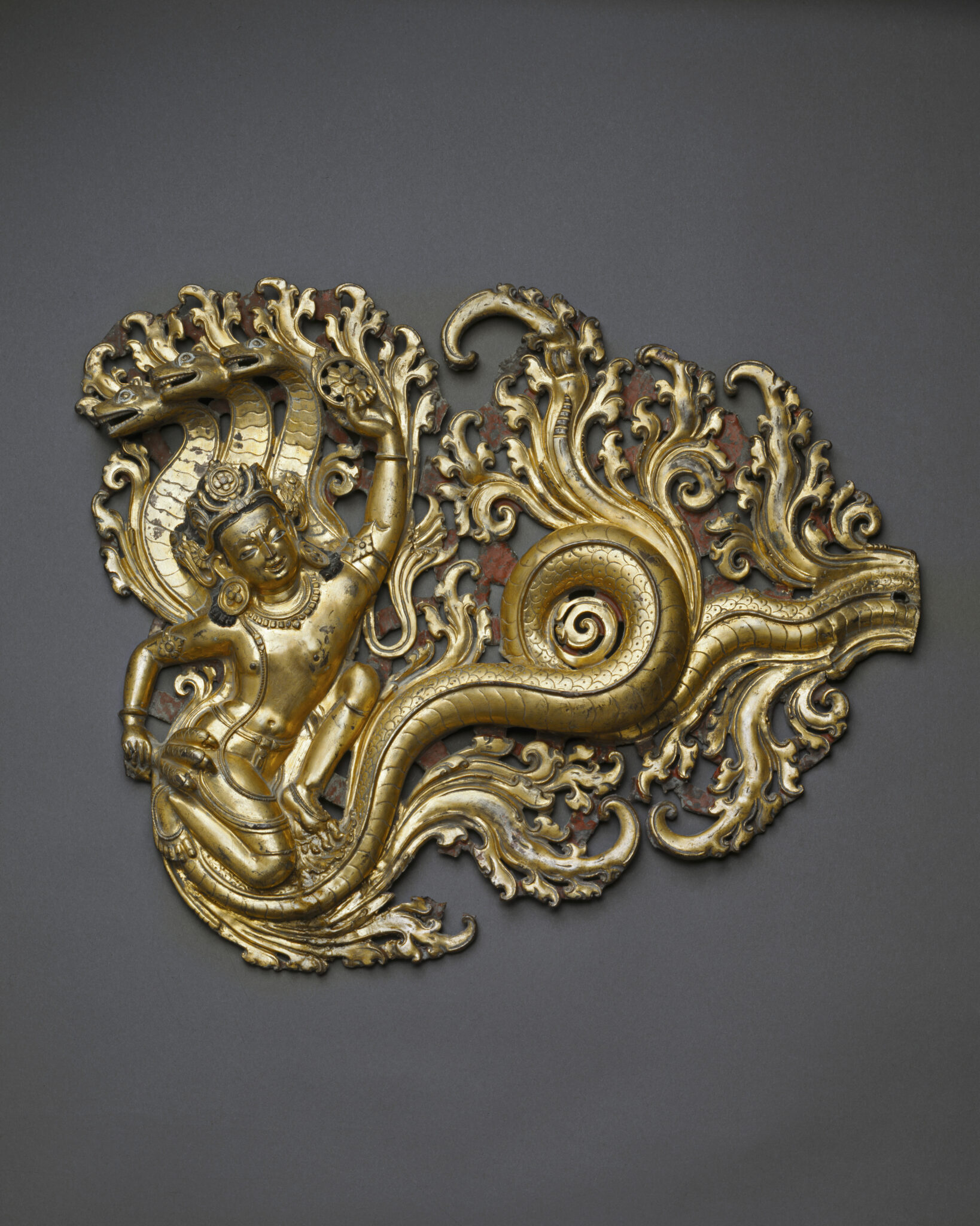 Gilt open metalwork depicting serpent deity hooded by three snakes, her tail curling amidst acanthus scrolls