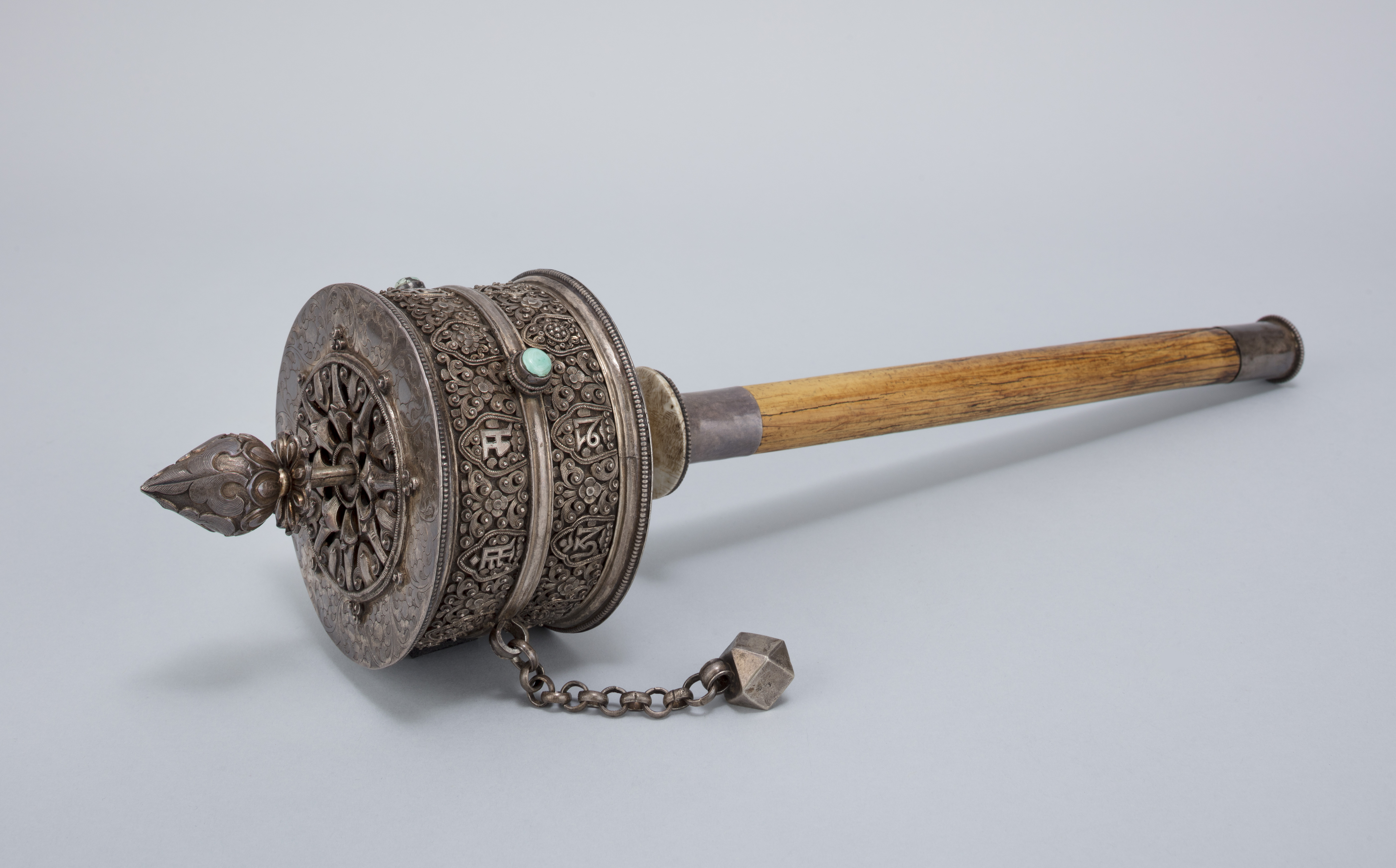 Silver religious implement with turquoise accents; ball and chain attached to rotating cylinder mounted on wooden handle