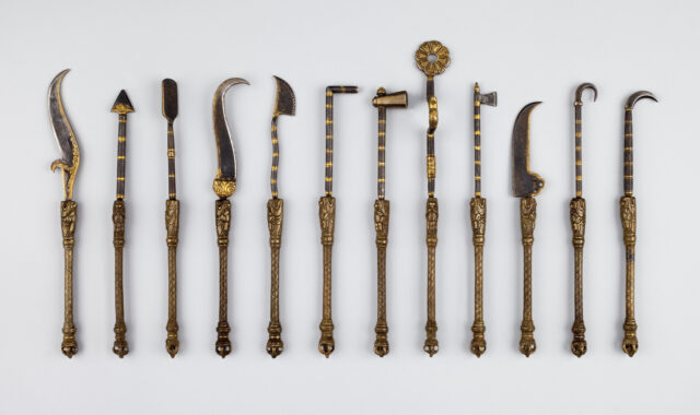 12 bronze-colored medical instruments with vajra-tipped handles: scalpels, probes, and hooks