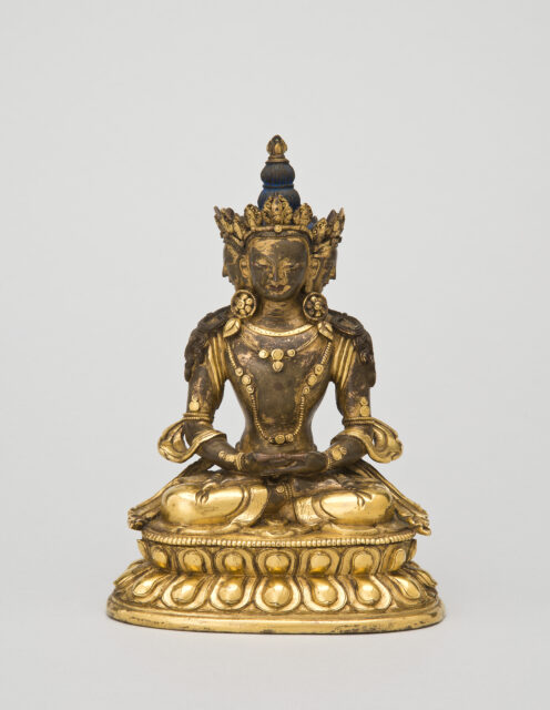 Patinated golden sculpture depicting Buddha wearing pointed crown and tall hairstyle seated in meditation