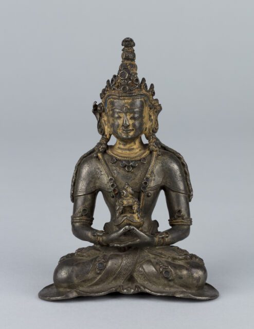 Patinated copper- and gold-colored statue depicting Buddha seated in meditation wearing crown and tall hairstyle