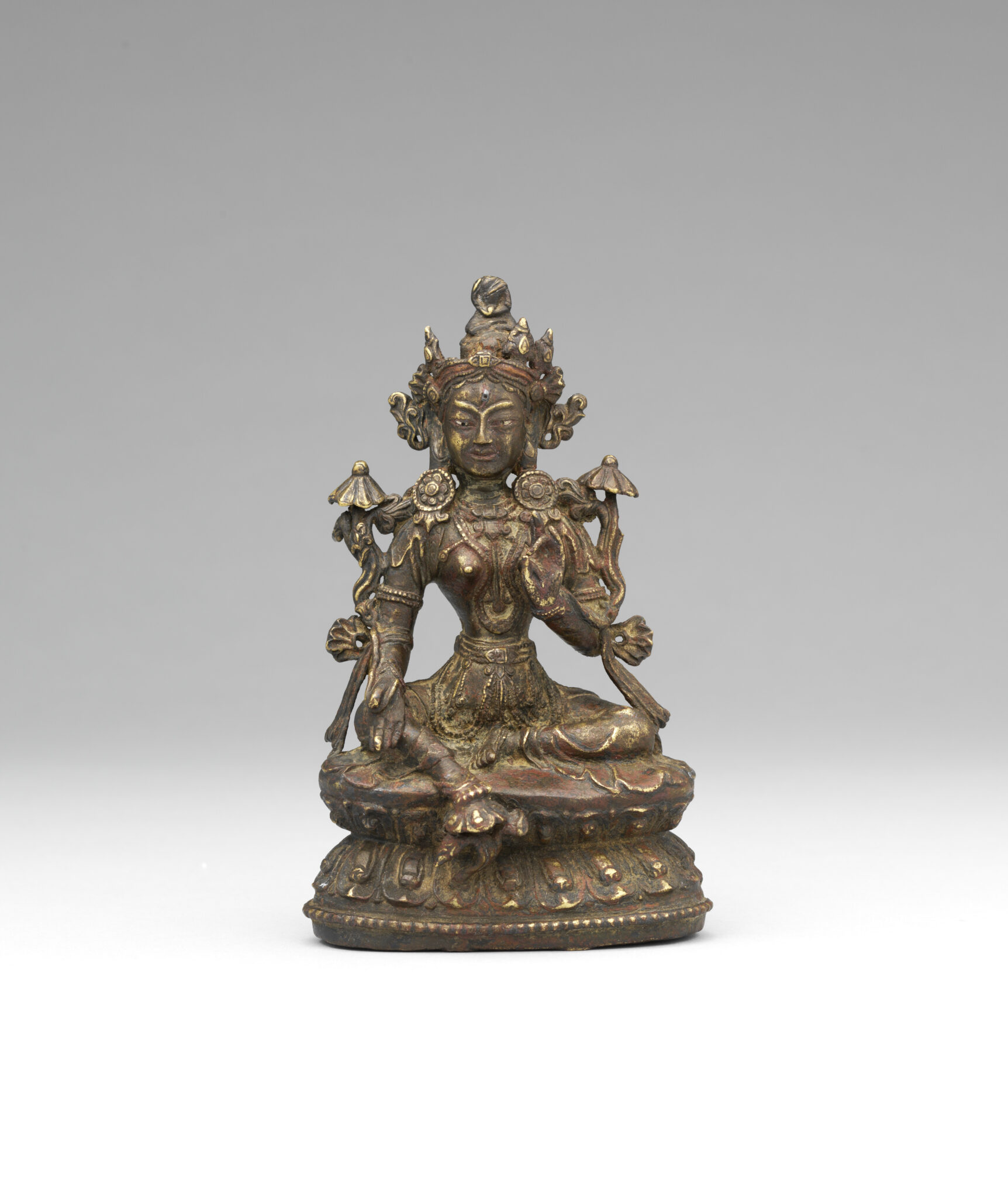 Patinated copper-colored statue depicting Bodhisattva holding hands in mudras, flanked by long-stemmed blossoms
