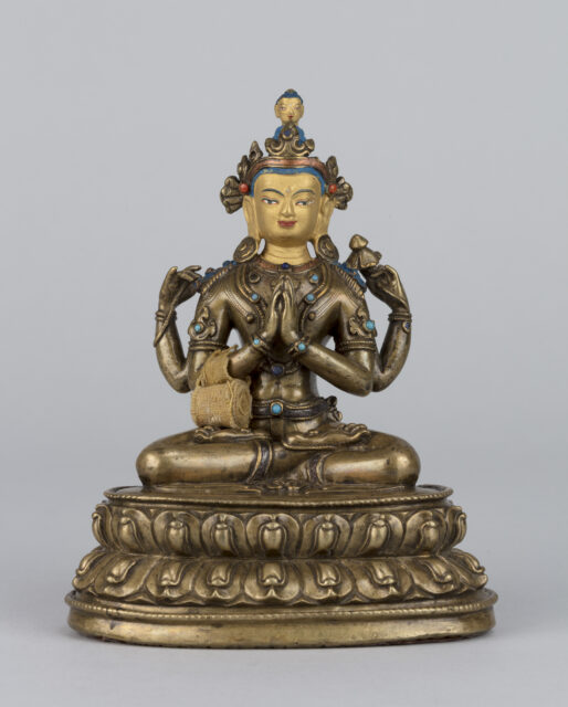 Bronze-colored sculpture depicting four-armed Bodhisattva seated on lotus pedestal; tightly wound textile scroll attached to front left arm
