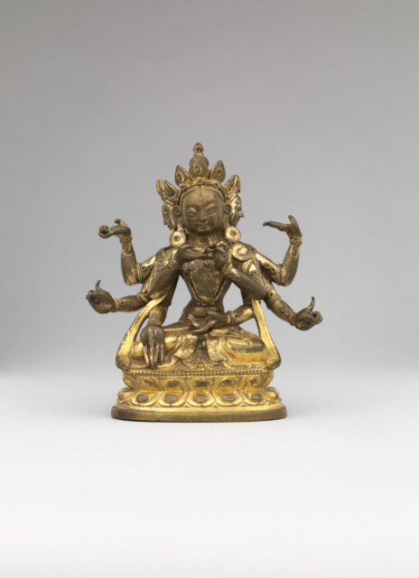 Tarnished golden statue depicting six-armed deity wearing pointed crown, posing hands in mudras