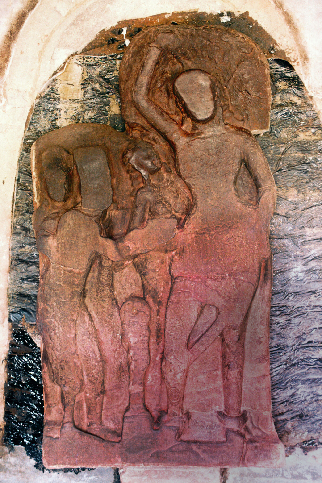 Brown-red relief against stone wall of featureless figure, arm raised, standing next to three smaller figures
