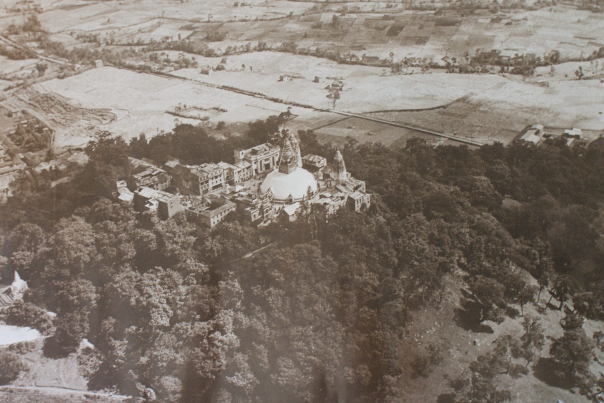 Sepia-toned aerial photograph of domed building in forest bordering grasslands and fields