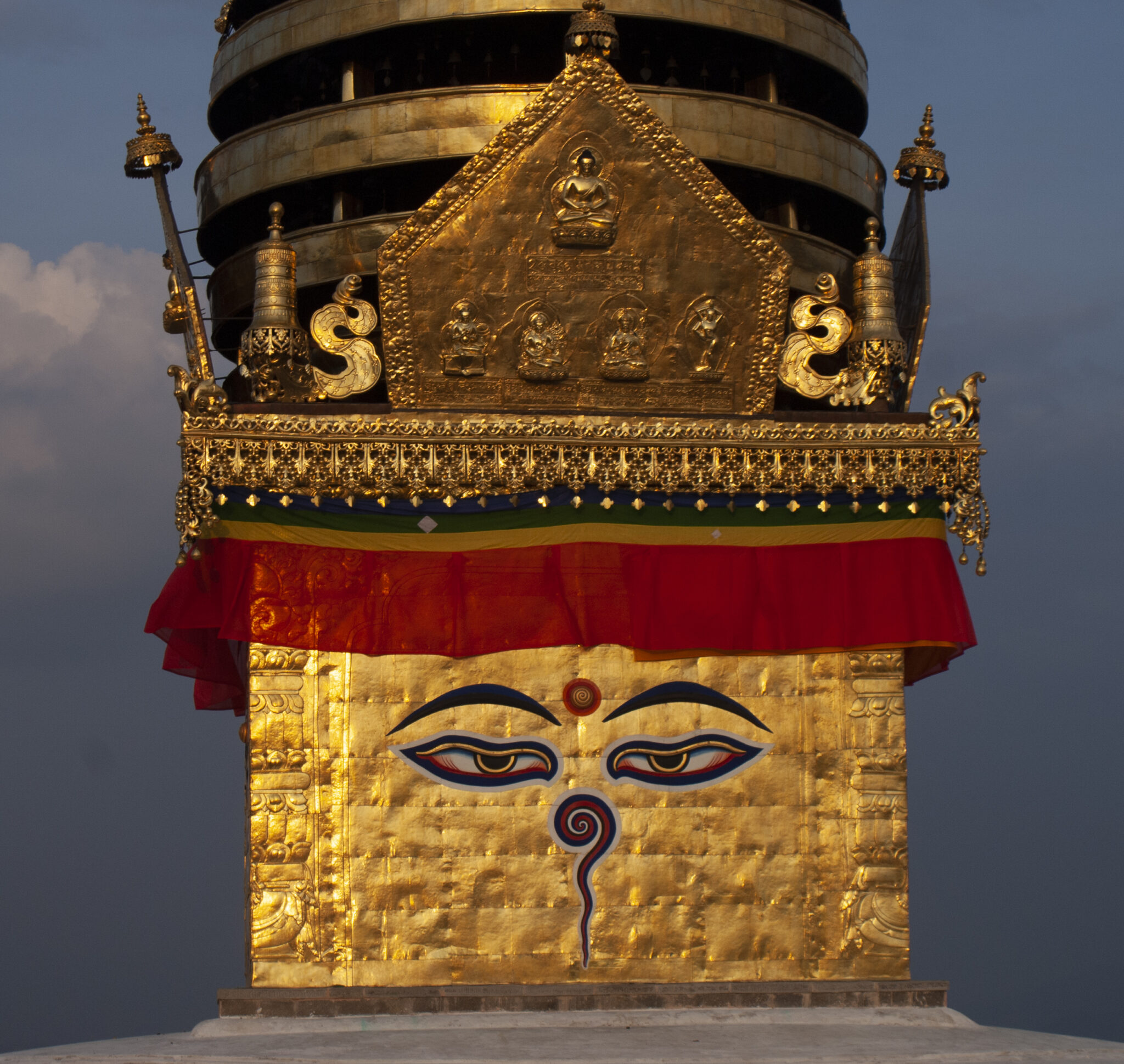Close view of golden stupa tower with red banner gleaming in sunlight against dark blue-grey clouds