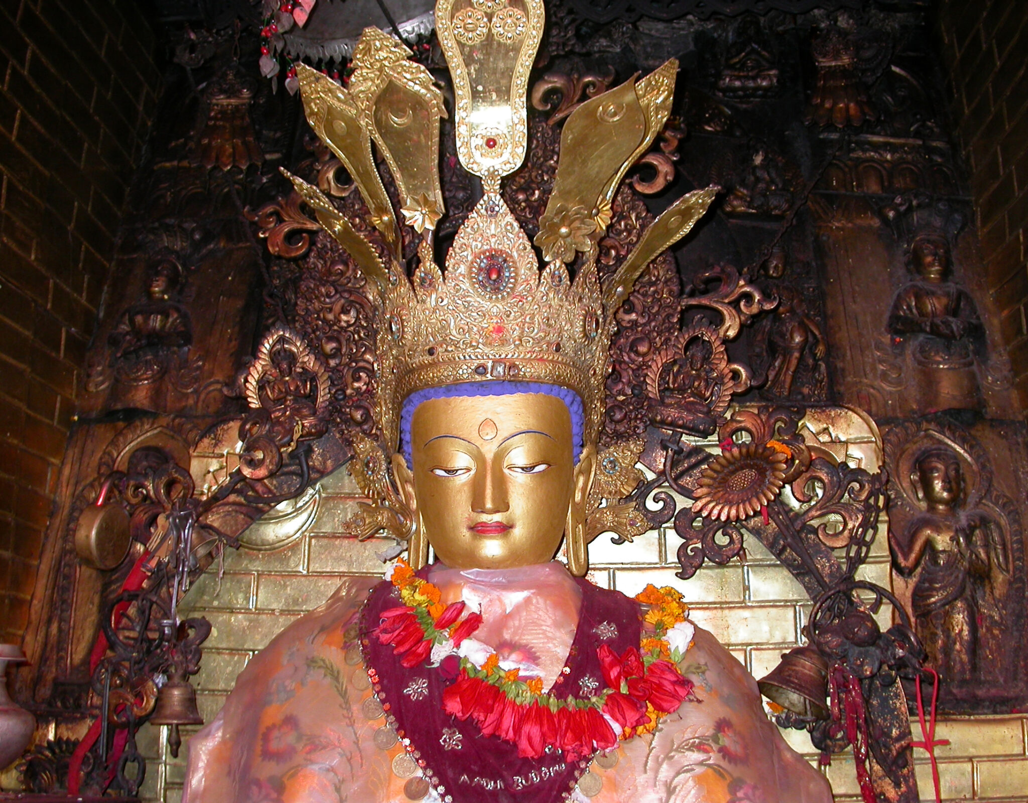 Crowned golden buddha in temple niche adorned with pink and purple textiles and flower garlands