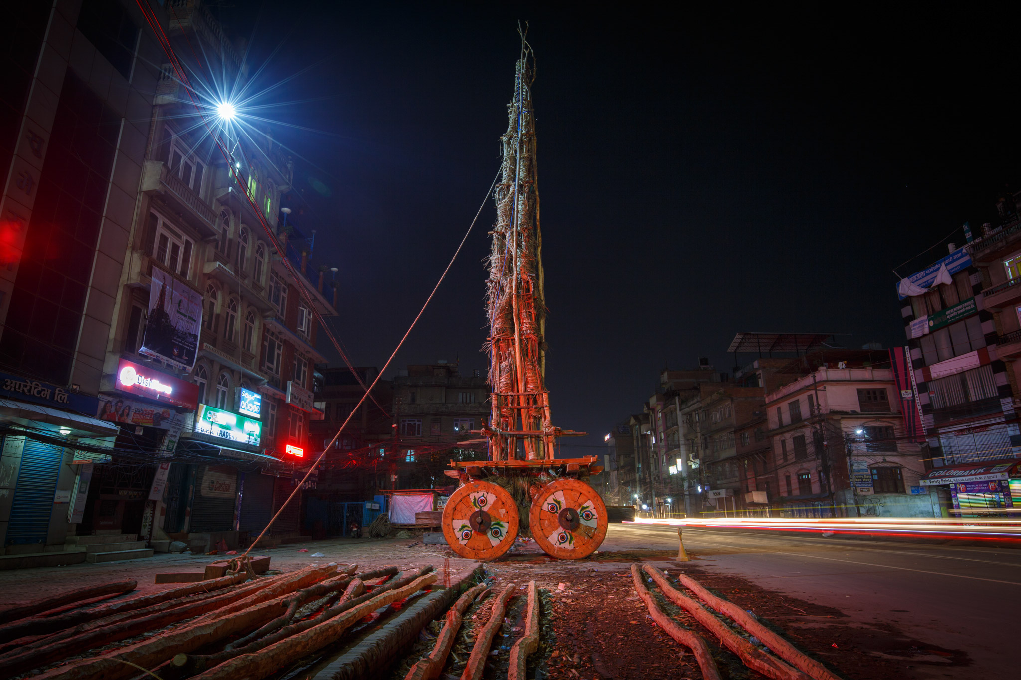 Tall spire made of textured materials rests on orange wheels beside city street at nighttime