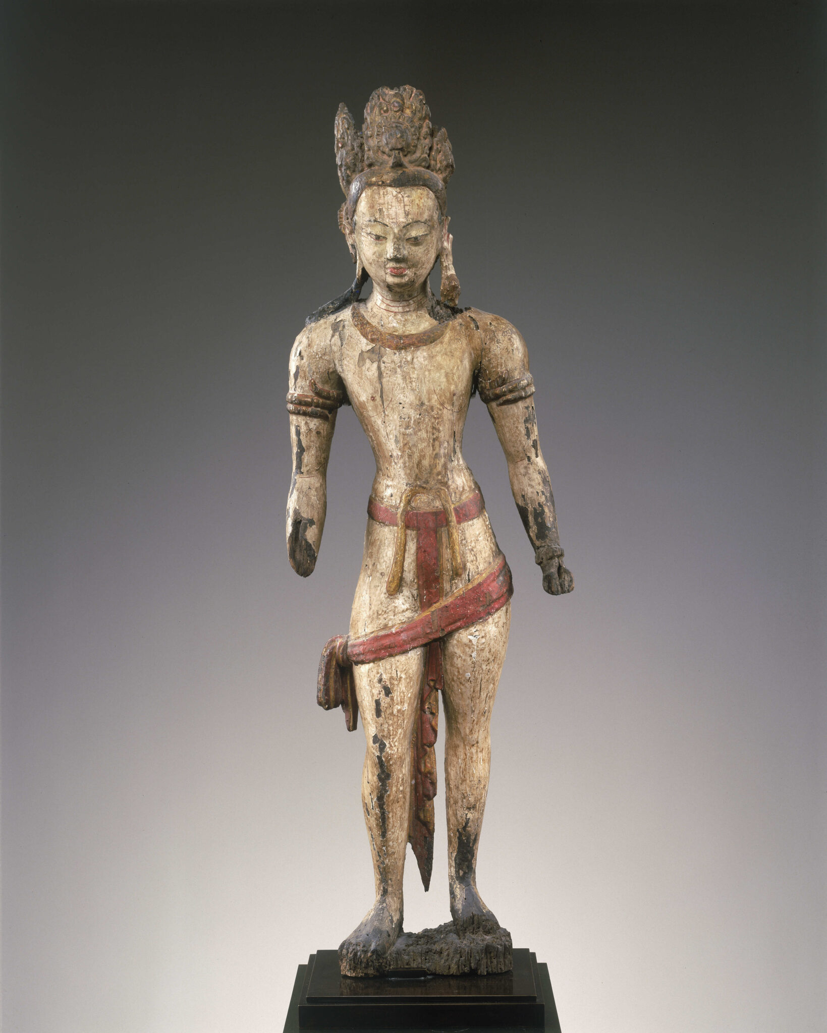 Wooden sculpture of crowned Bodhisattva with pinched waist and red textile strips at midsection; hands and left forearm missing