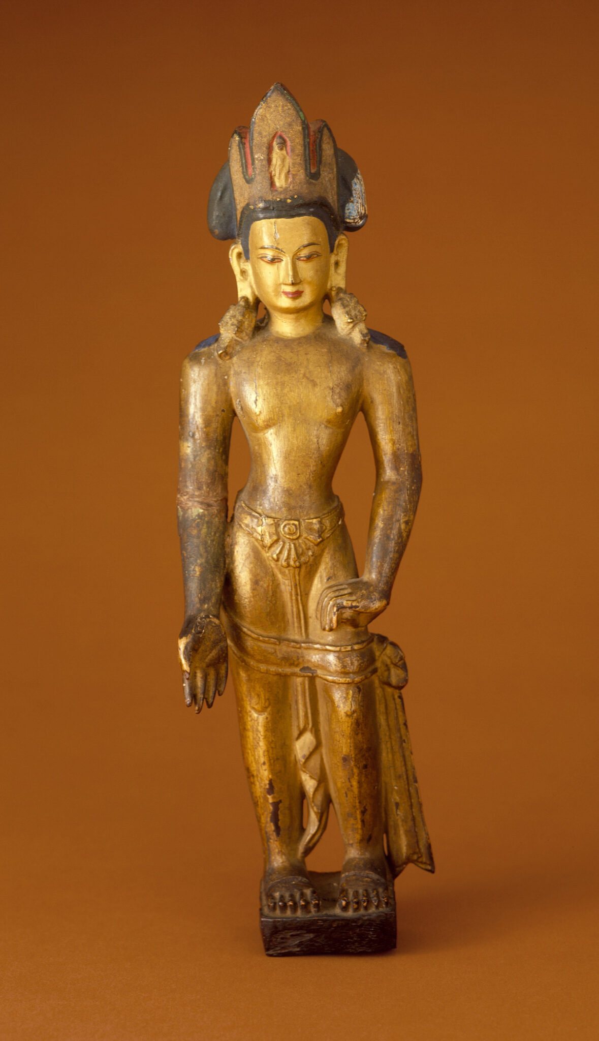 Golden statuette of crowned deity with left palm facing viewer and right hand on hip