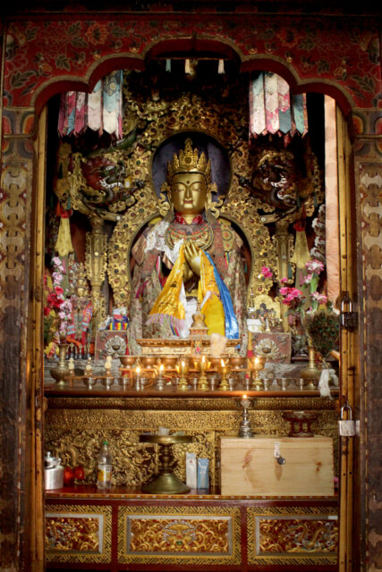 Three-quarter bust of Buddha in ornately carved niche surrounded by colorful banners and offerings