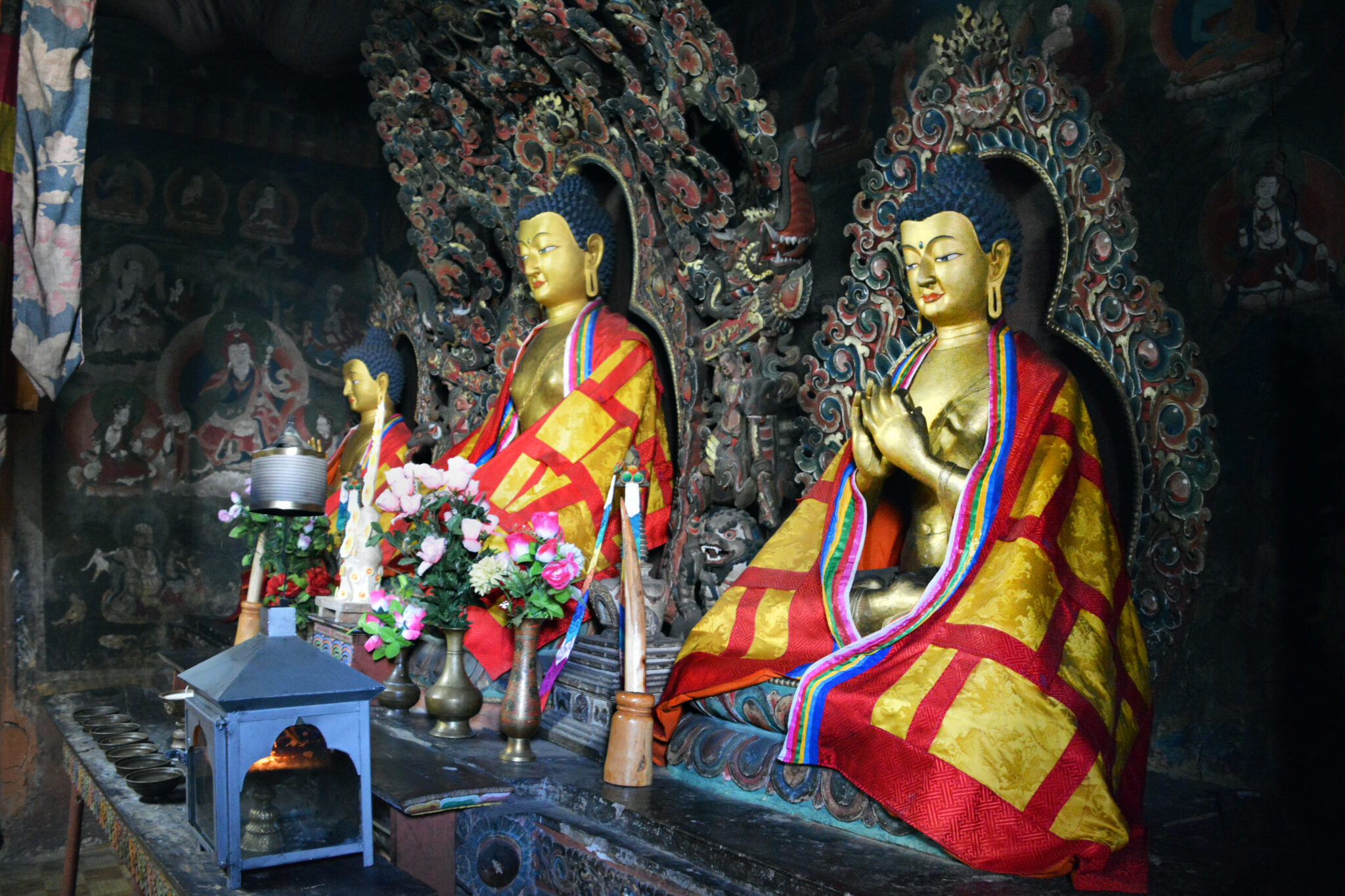 Three golden Buddhas wearing saffron and red cloaks seated before mandorlas in niche decorated with murals