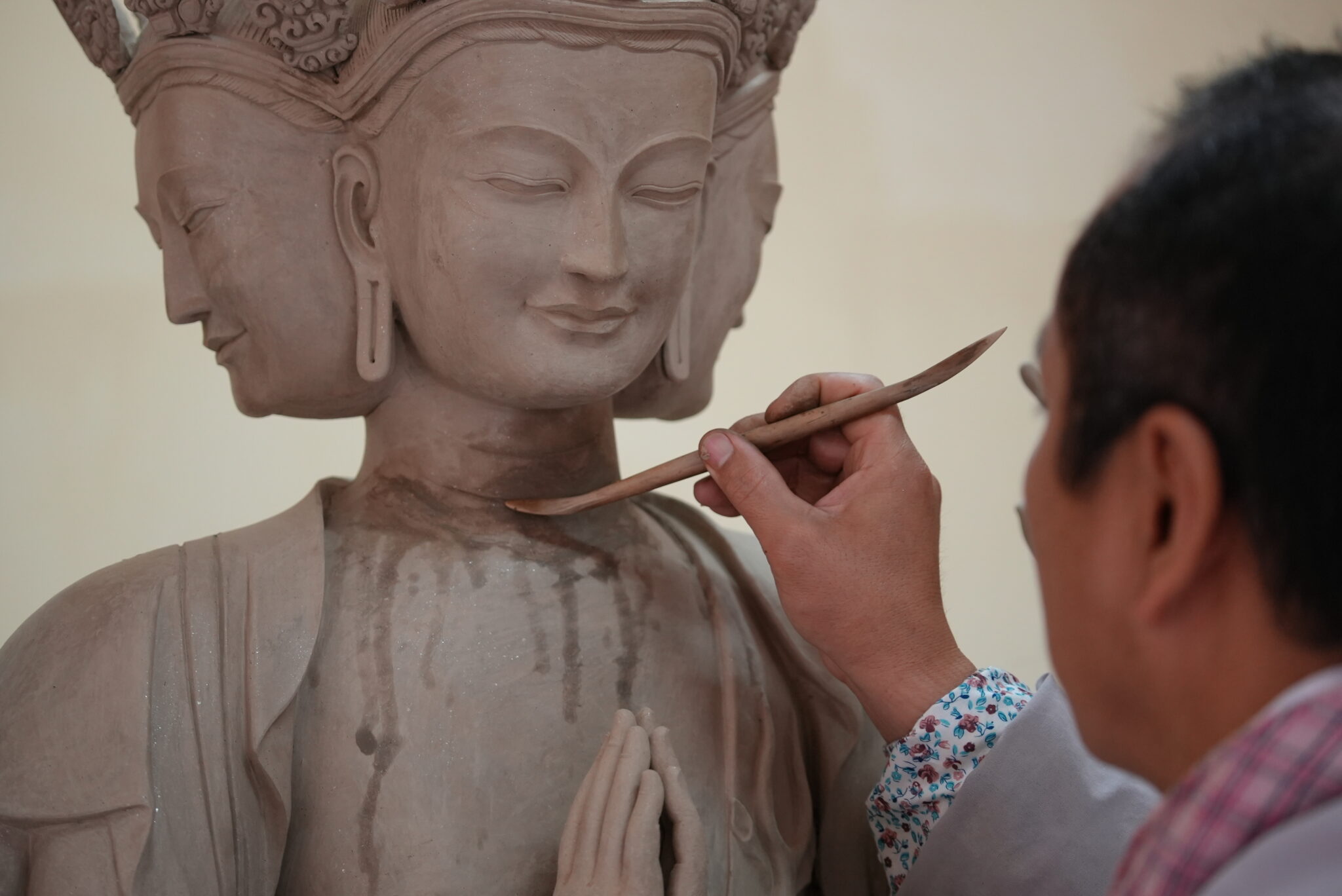 Sculptor works carefully with long, thin tool on unfinished sculpture of three-faced deity