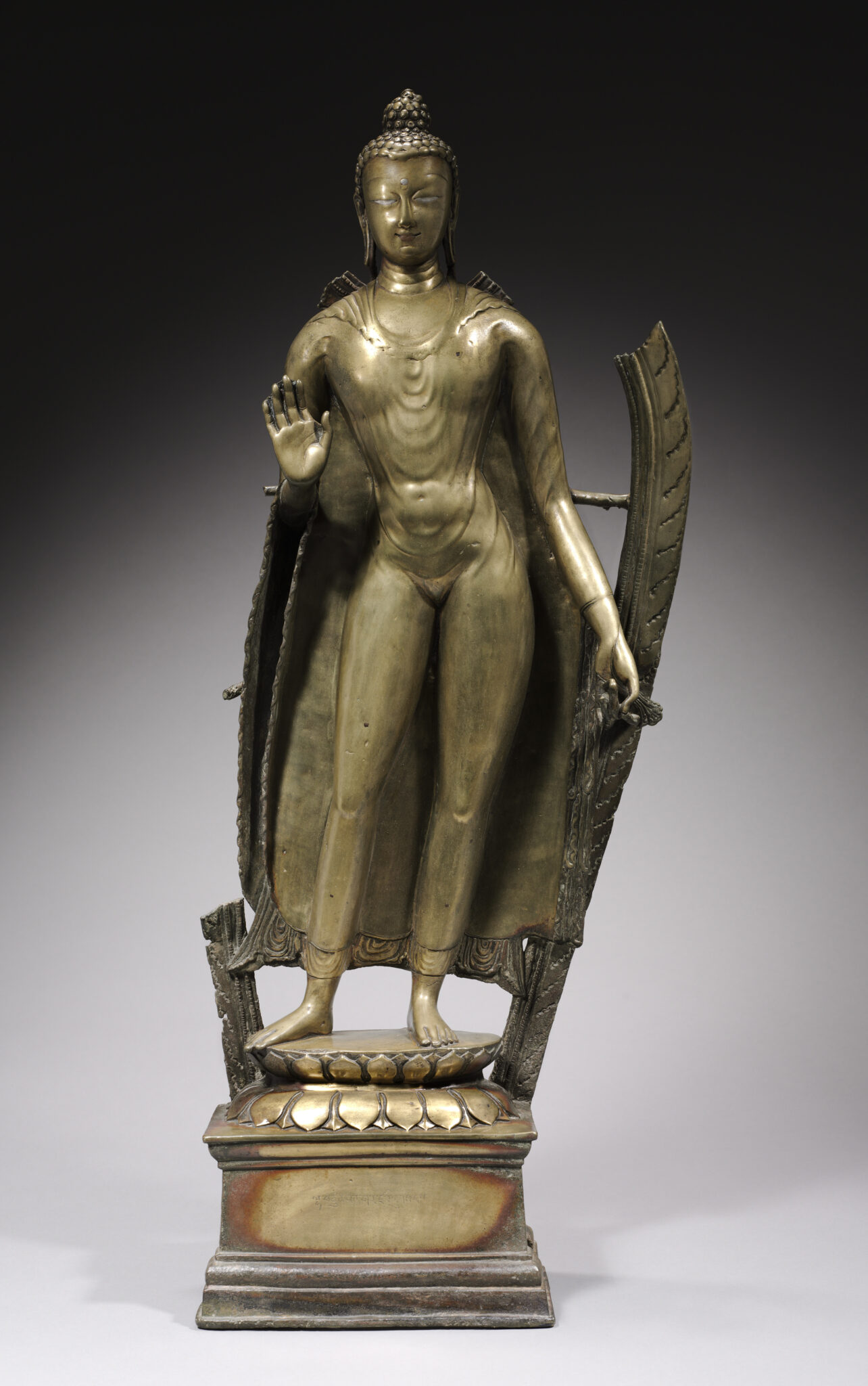 Brass statue of Buddha standing in contrapposto before damaged mandorla