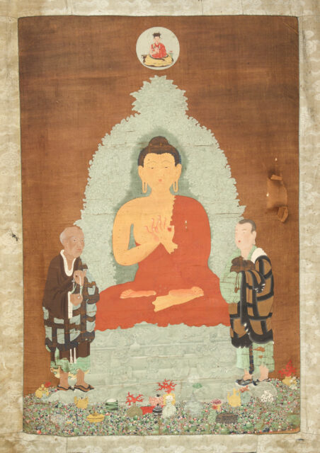 Buddha in orange robe sits cross-legged on grisaille throne while flanked by two smaller men in patchwork robes