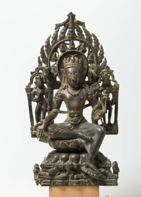 Dark-brown statue of bodhisattva seated on lotus pedestal before mandorla decorated with various deities