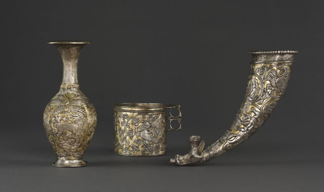 Three highly decorated silver drinking vessels: one tall with long, thin neck; one short and cylindrical; one horn-shaped