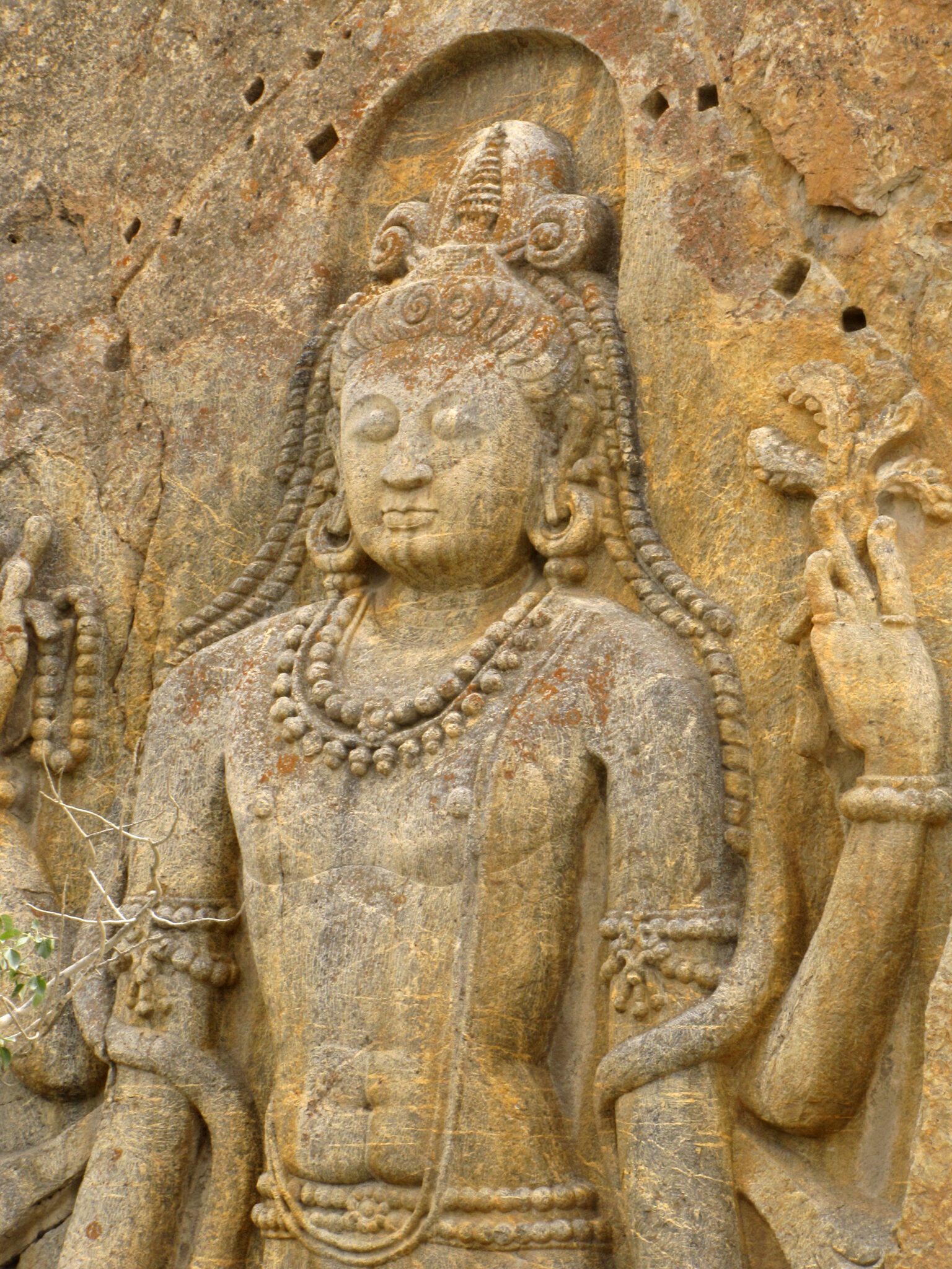 Medium view of torso and head of Bodhisattva with eyes closed; relief carved in yellow-brown stone