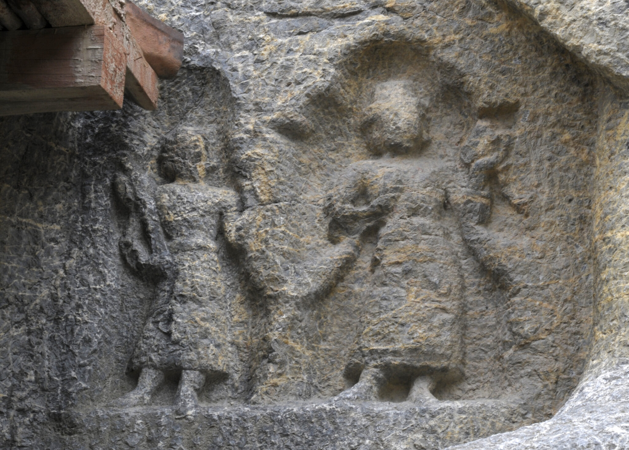 Weathered and abraded rock carving depicting two skirted figures standing inside shallow niches