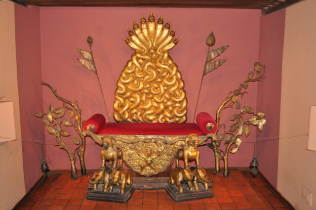 Red-upholstered golden throne featuring backrest with coiled-snake motif and legs made of animals standing atop one another