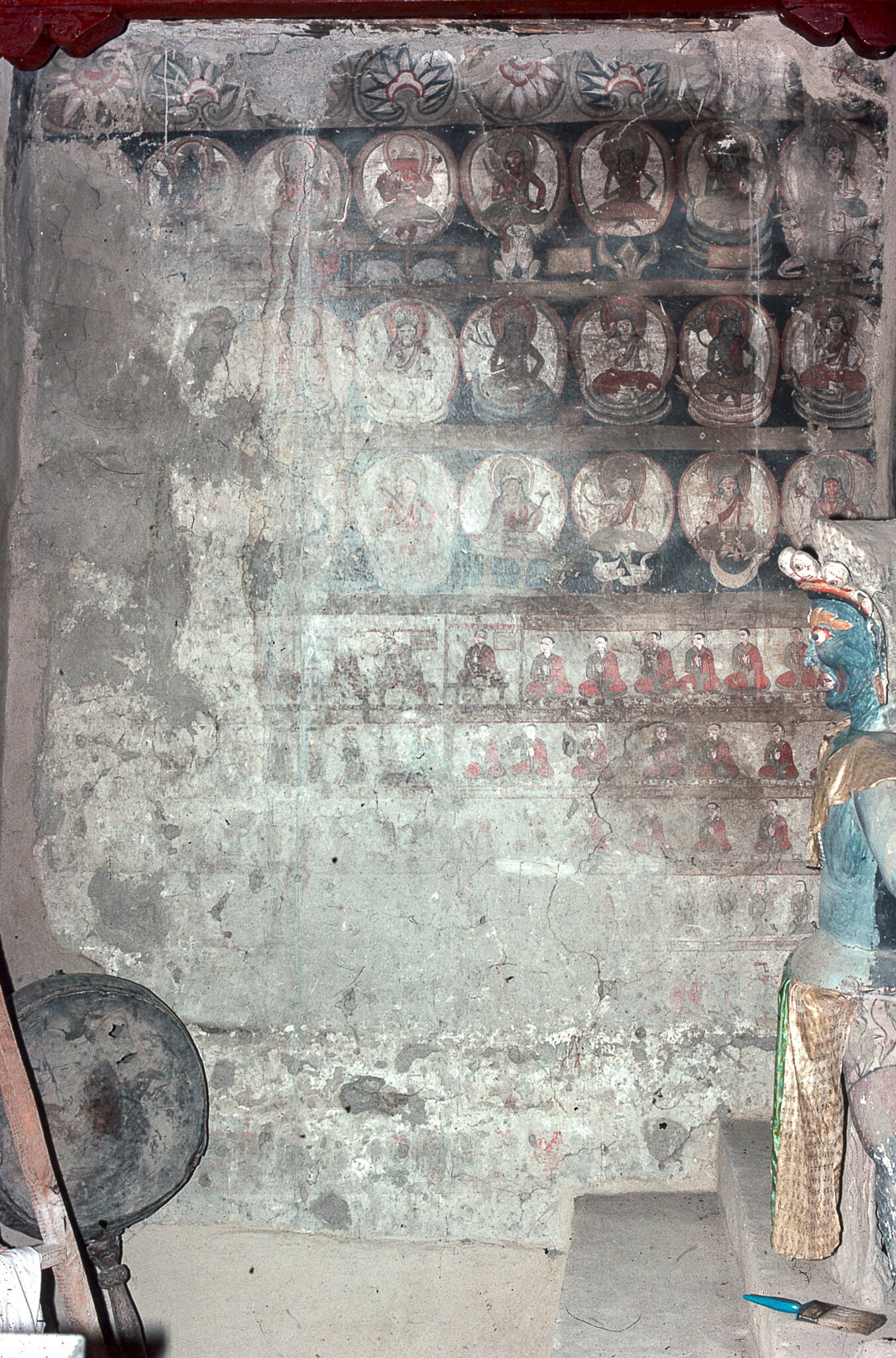 Damaged mural depicting three registers of seated deities above multiple registers of seated donor figures
