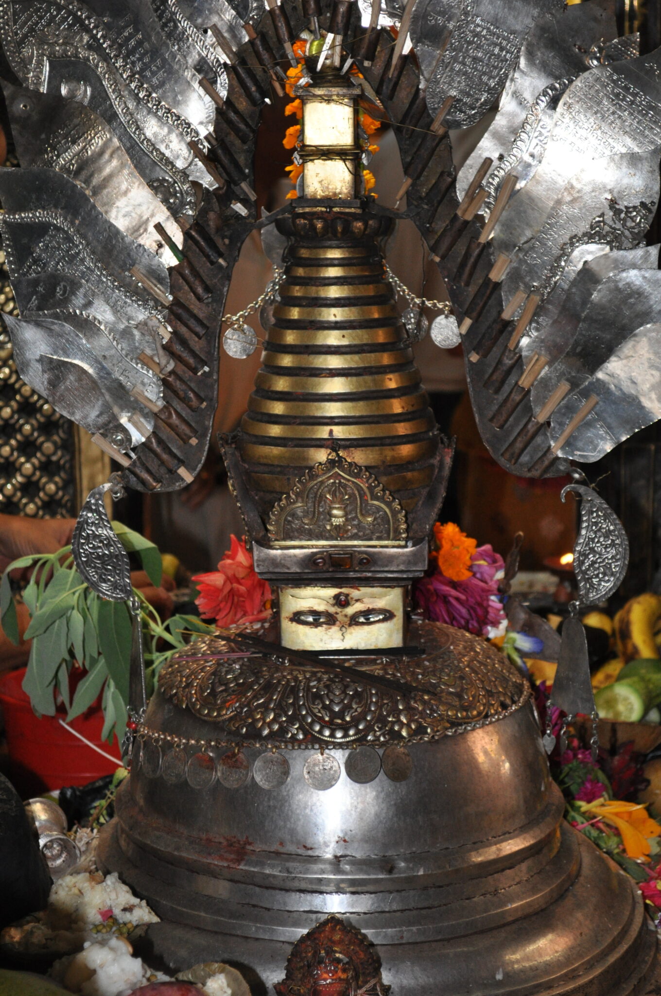 Silver- and bronze-colored metal devotional object in stupa shape; topped with silver feather-shaped ornaments