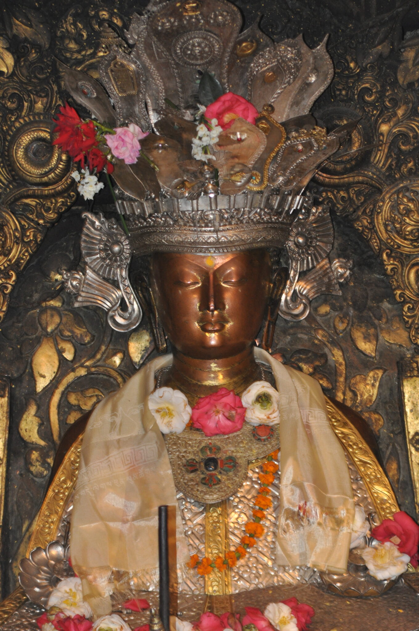 Medium view of Buddha statue's upper body with silver crown, copper face, and textile adornments