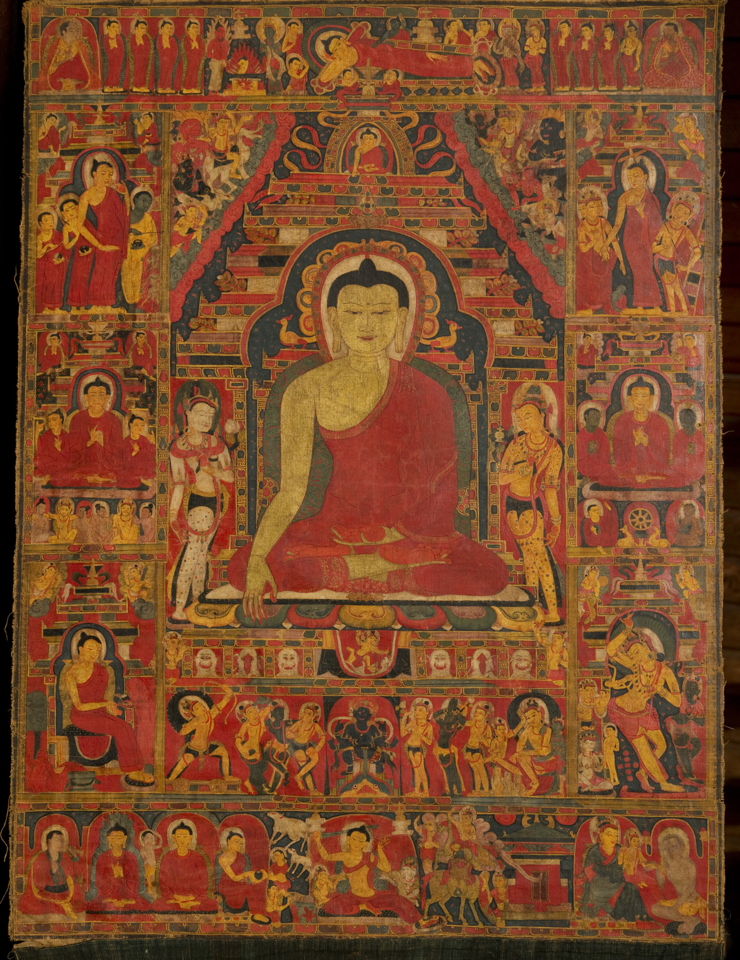 Painting in crimson-red and burnt orange depicting seated Buddha surrounded by profusion of scenes and figures arranged in five registers
