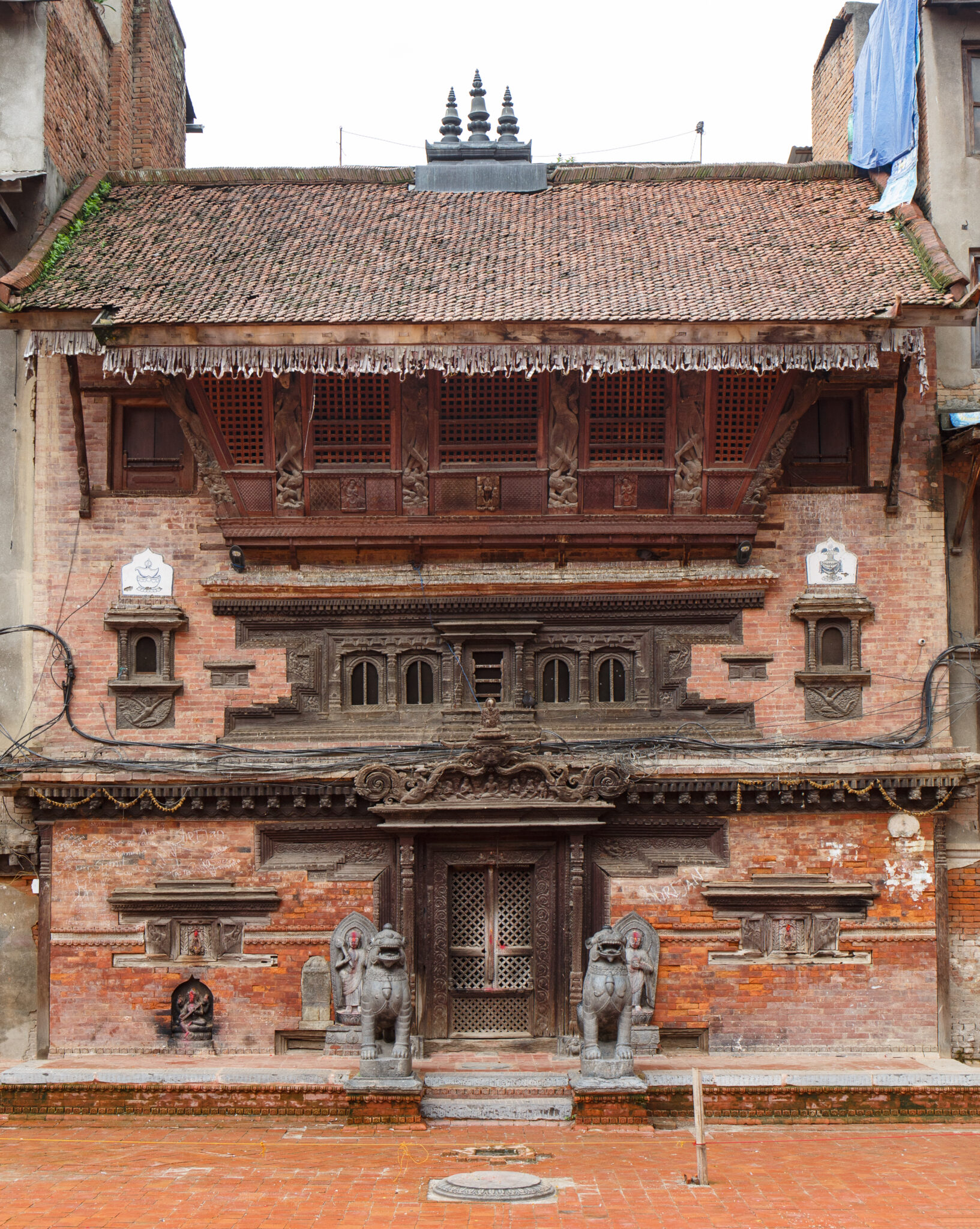 Facade of three-story orange-brown brick building with densely carved woodwork at door, windows, eaves, and lintels