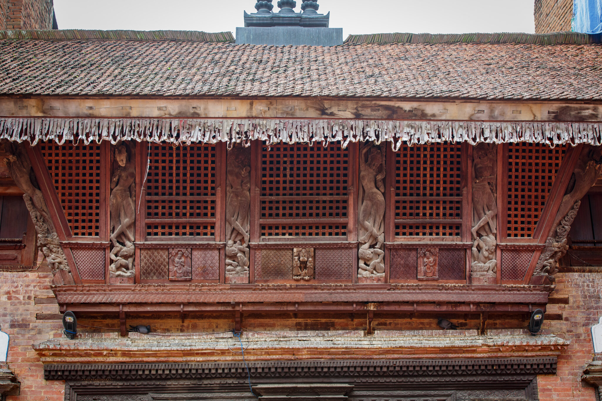 Medium view of five screened windows separated by carved figures on upper story of brick building