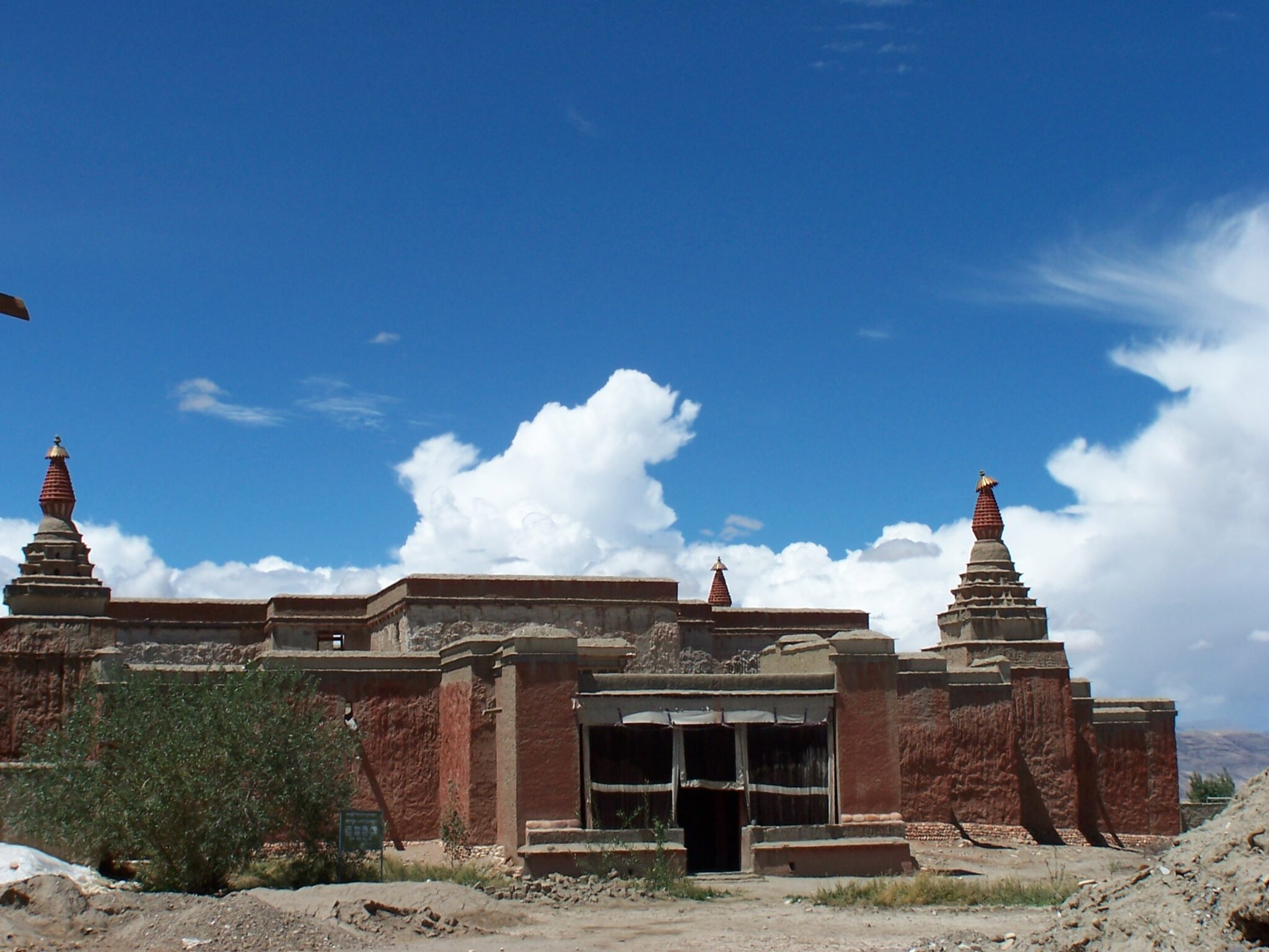 Medium view under blue sky of low-slung rust-red temple building featuring stupas at corners of roof