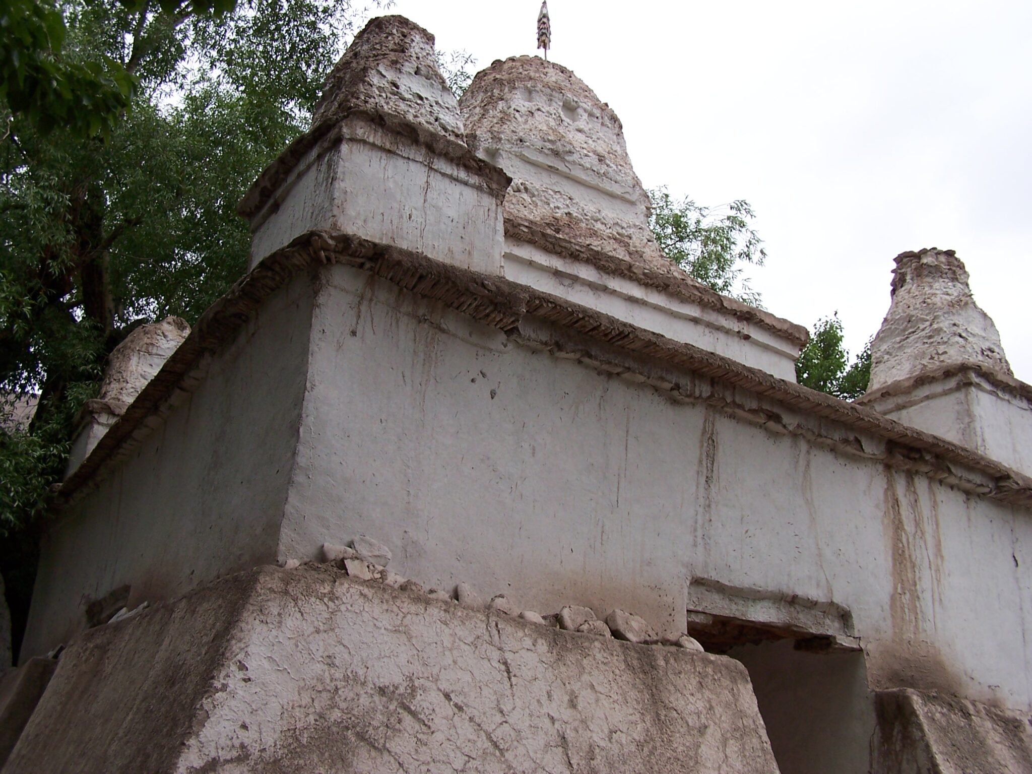 Close view from below of white stupa on square base with eroded, crumbling towers