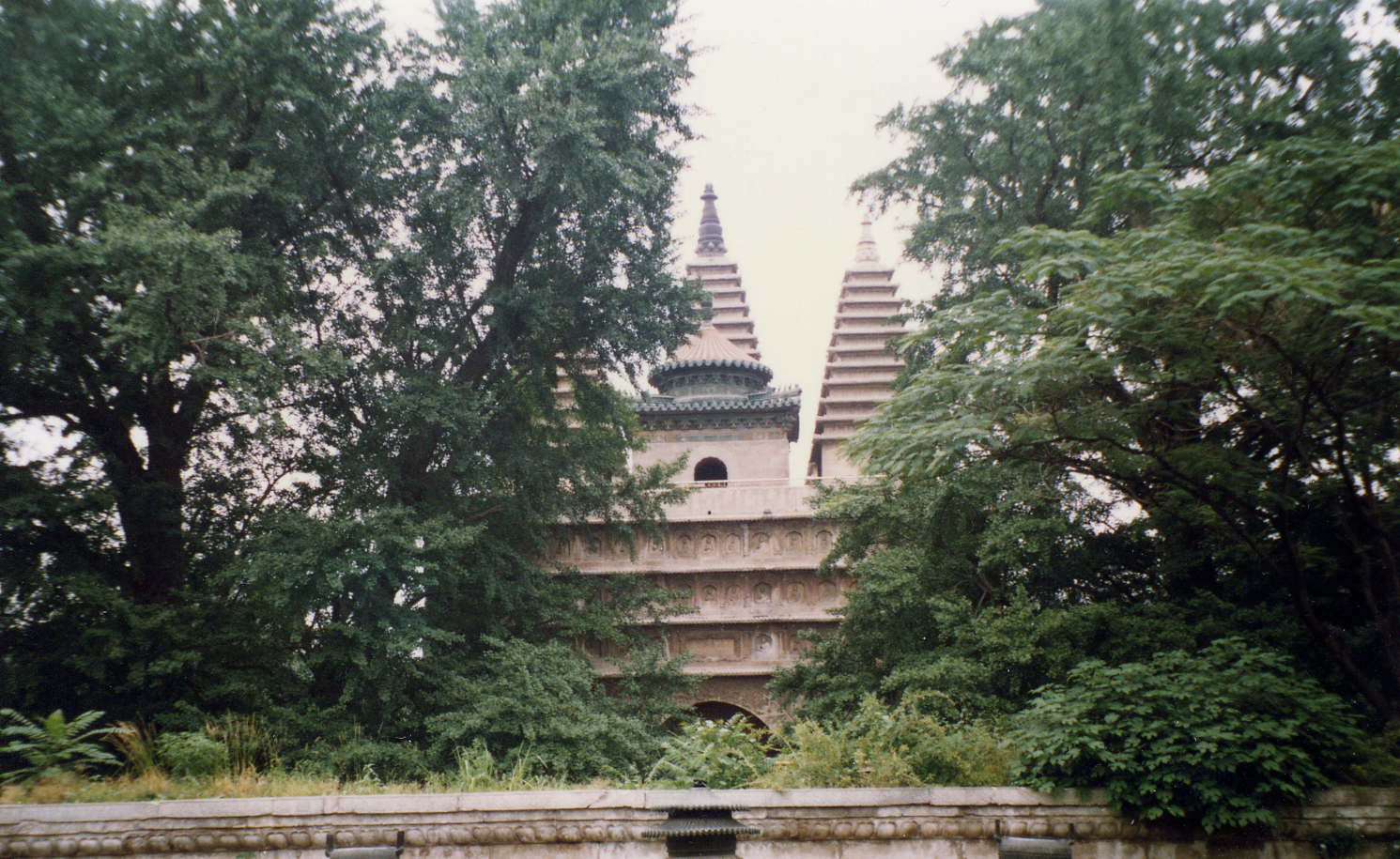 View through trees of building featuring three tapered towers and smaller central tower with conical roof