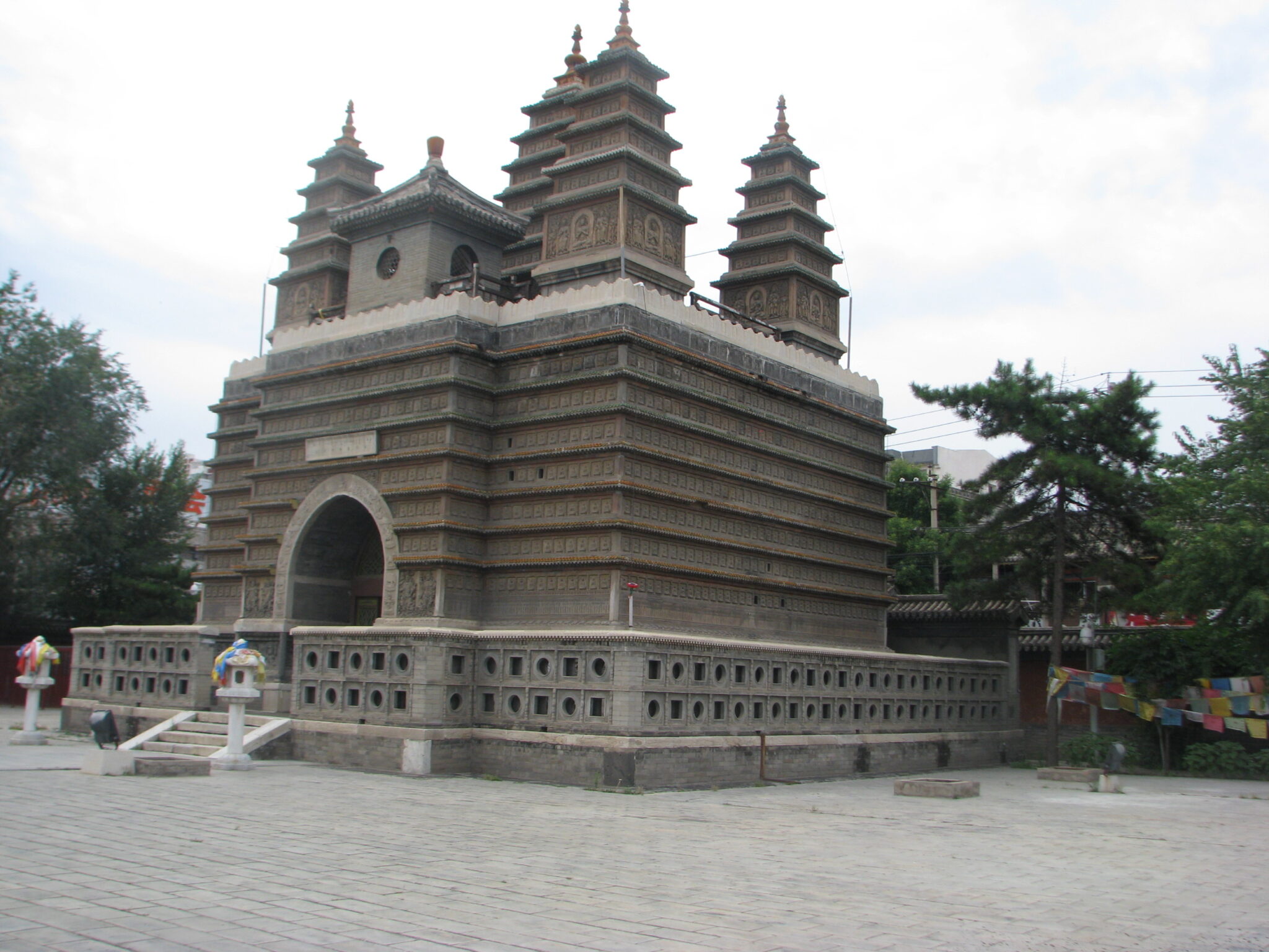 Wide view of gray stone building featuring square base with repeated horizontal moldings and multiple pagodas on roof