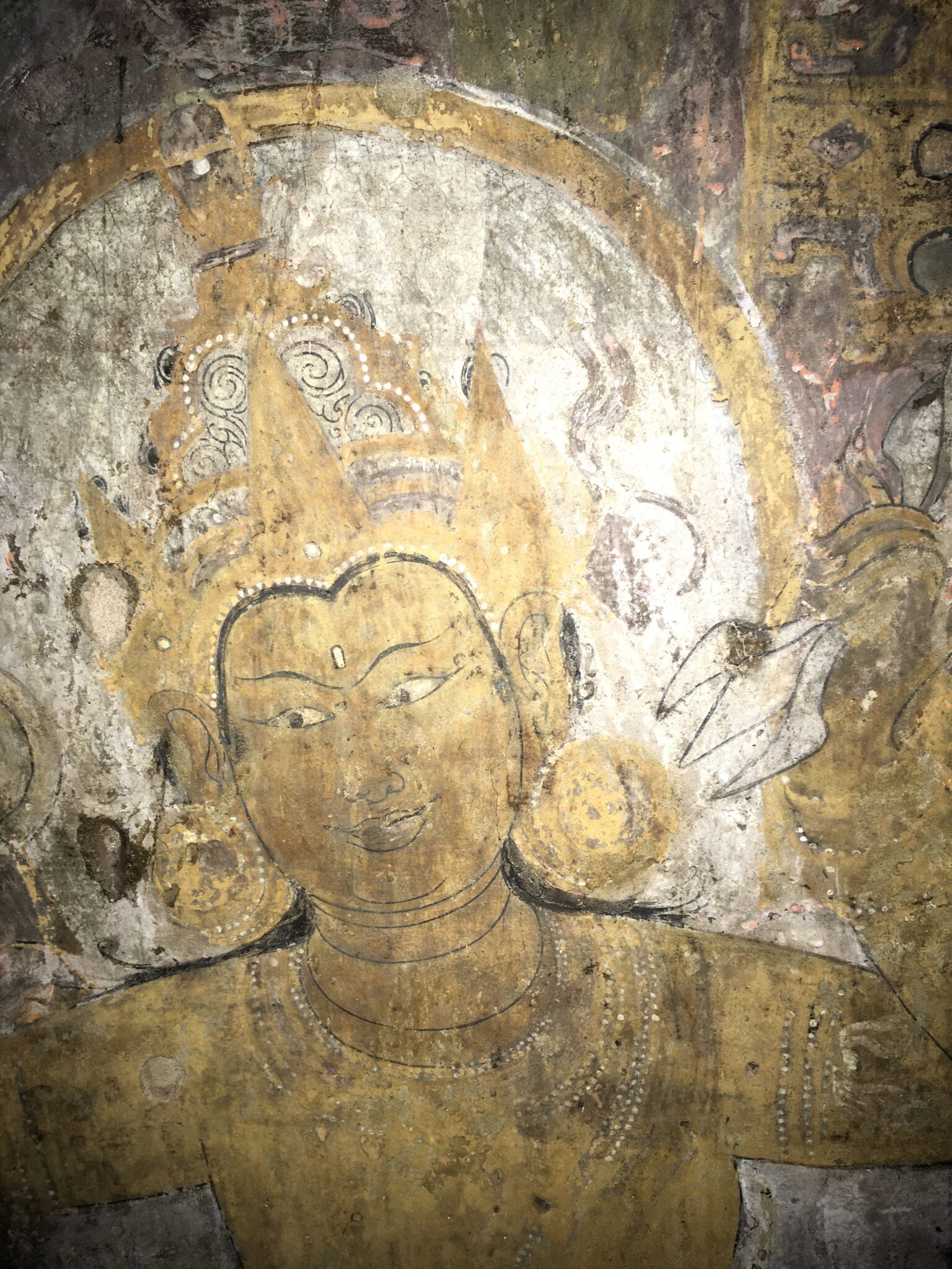 Head and shoulders of crowned Bodhisattva with yellow skin holding blossom; detail of faded mural