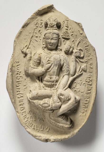 Beige ovoid relief depicting four-armed deity surrounded by symbolic motifs and Tibetan text
