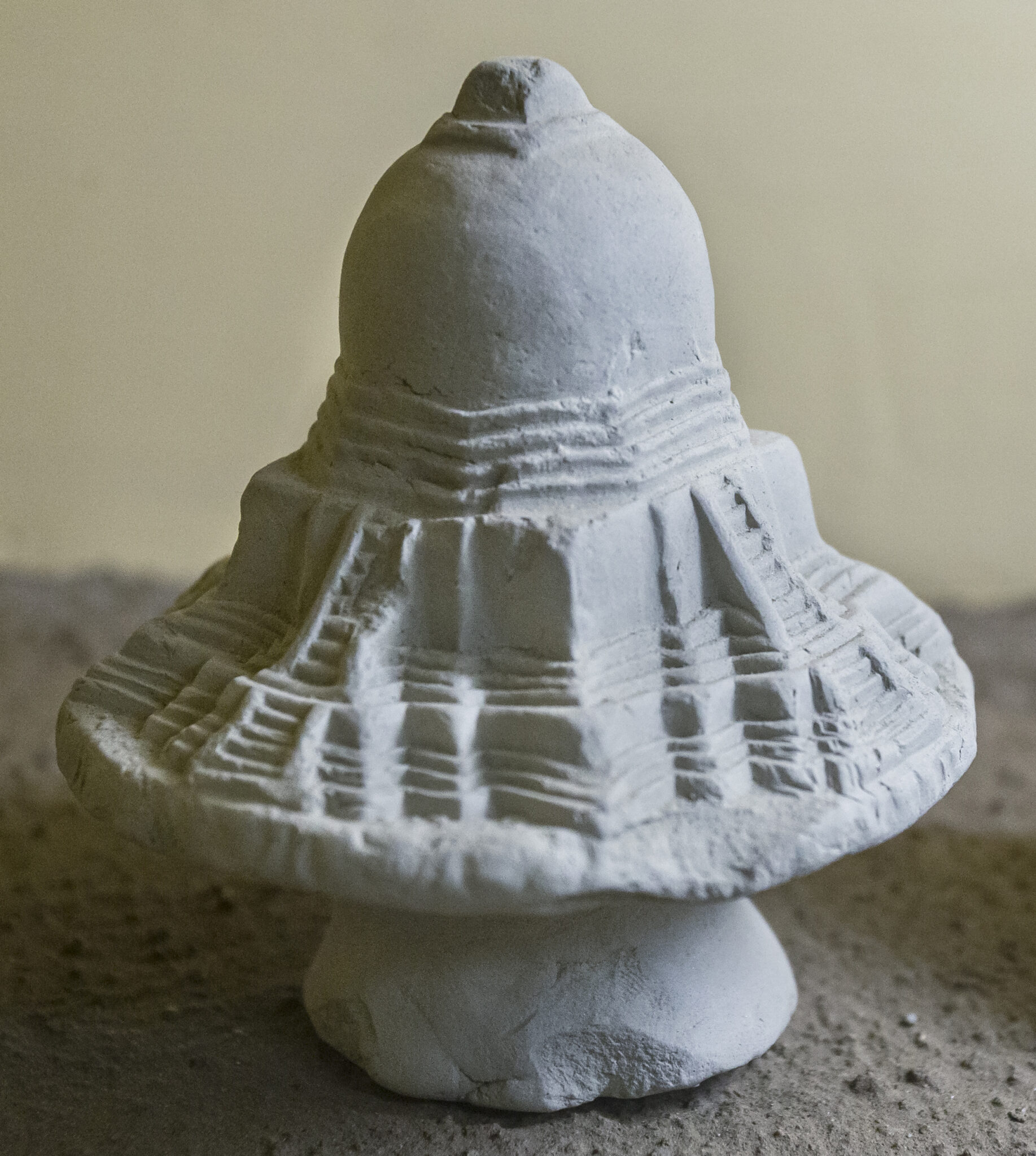 Close view of light-gray earthenware model of stupa featuring clearly demarcated staircases and moldings
