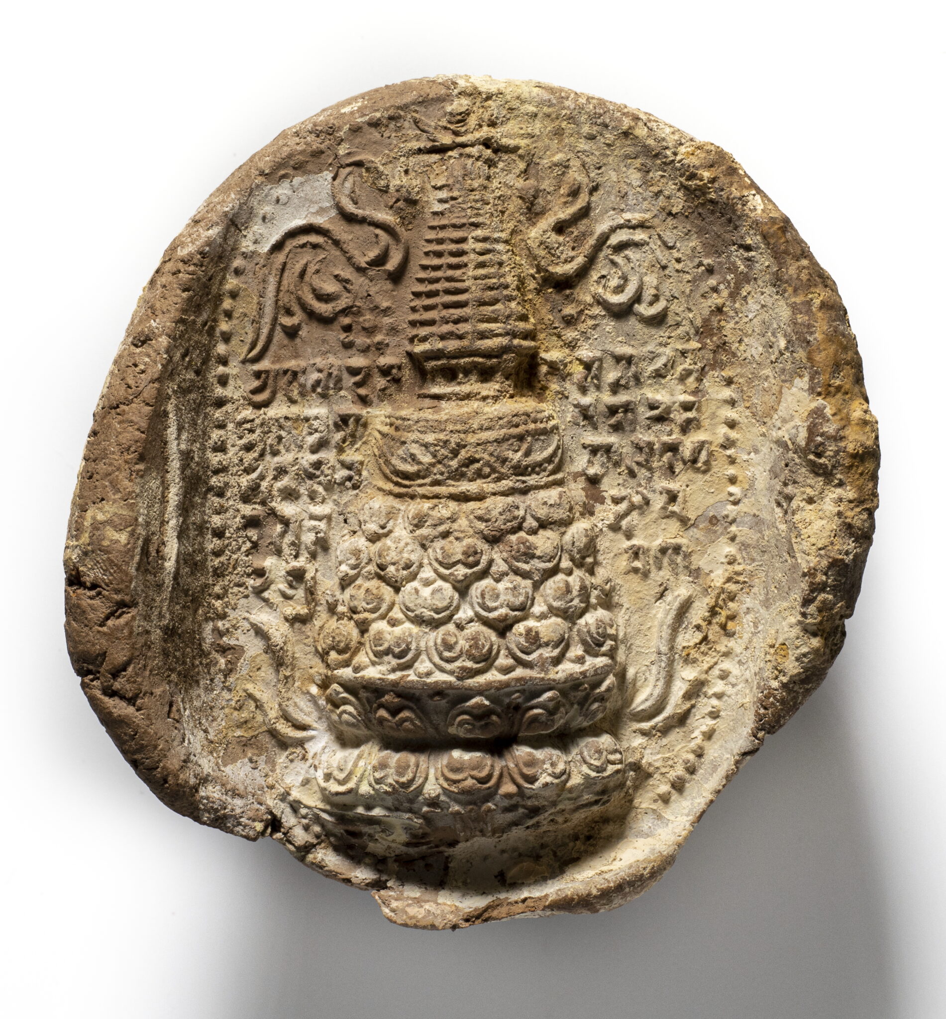 Mottled brown clay roundel featuring stupa decorated with lotus motif and banners amid Tibetan text